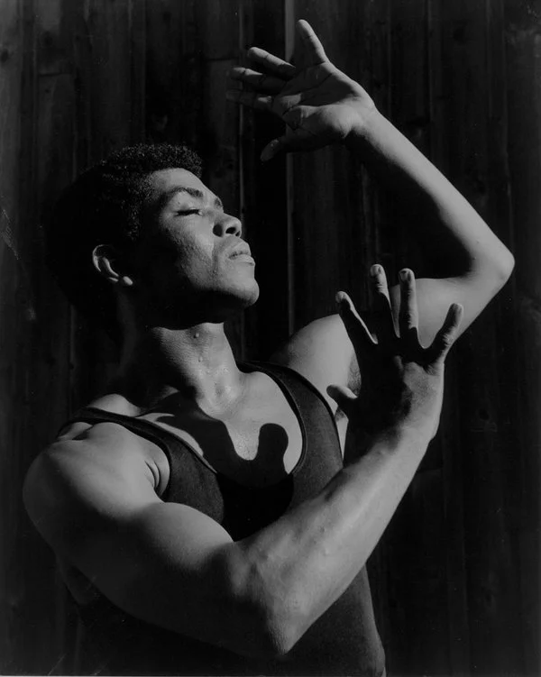 A black & white portrait of a young African American man, posing as if mid-dance.