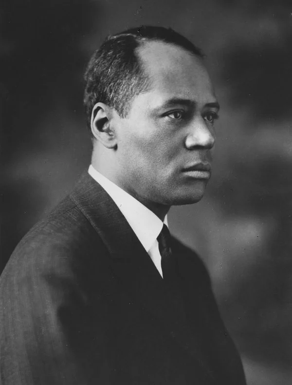 A black & white portrait of an African American man in a dark suit and tie.