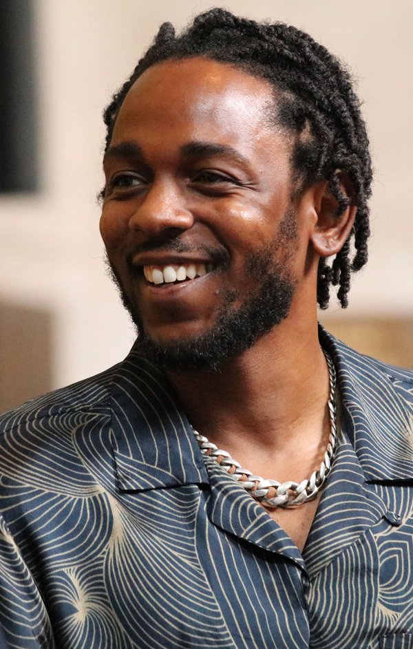 A color photo of a smiling African American man wearing a silver chain and a blue-and-gold patterned shirt.